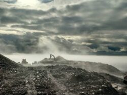 Heavy machinery operates amid a dusty landscape under a dramatic sky with sunbeams piercing through the clouds.