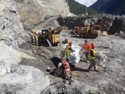 Workers in high visibility safety gear handling materials at a construction site with heavy machinery in operation.