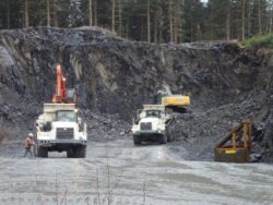 Heavy machinery operating in a quarry with rocky terrain and standing water.