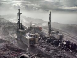 Drill rigs operating in a misty, rocky mining environment.