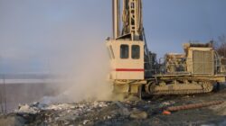 A drilling rig operating in a cold environment with visible steam or exhaust, likely indicating active work.