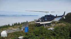 A helicopter positioned atop a mountain with equipment off to the left hand side.