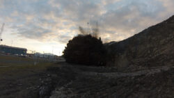 Dirt and debris are erupting from the ground at a construction site against an evening sky.