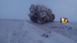 An explosion producing a large plume of smoke and flames erupts on a snow-covered landscape.