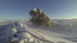 Demolition dust cloud among snowcapped mountains.