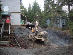 Construction equipment beside a muddy excavation site near a building with stair access.