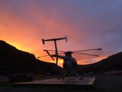 A helicopter on a landing pad at twilight with a fiery orange sky in the background.