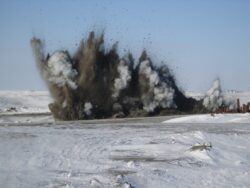 Controlled explosion creating a large plume of smoke and debris against a snowy landscape.