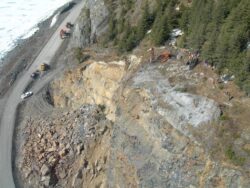 An aerial view of a road construction site on a mountainside, with heavy machinery and workers present.
